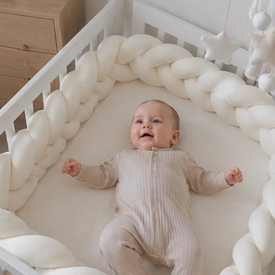 Tour de lit tressé beige avec bébé souriant allongé les bras ouverts