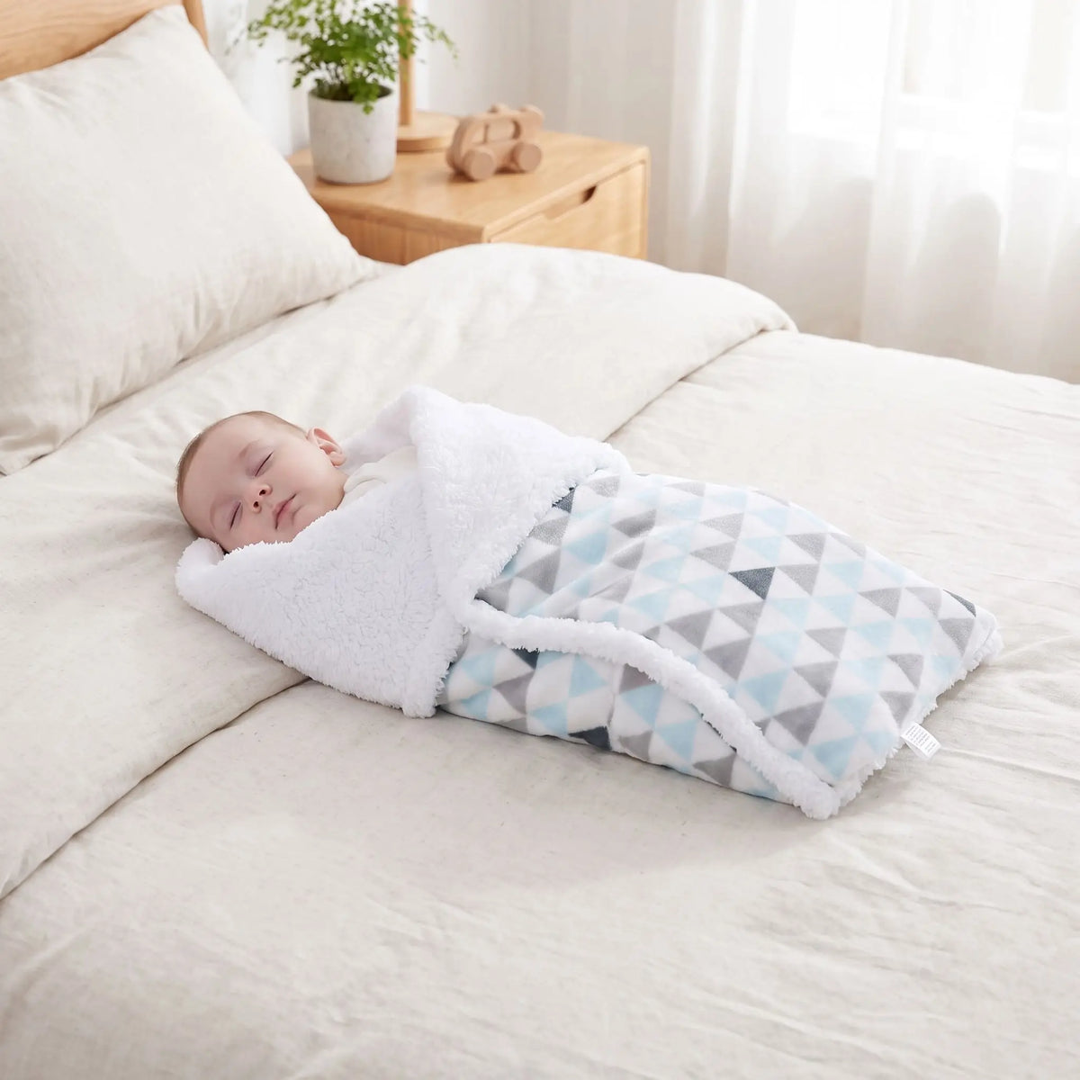 Couverture bébé triangles bleu gris emmaillotant nouveau-né endormi sur lit cosy

