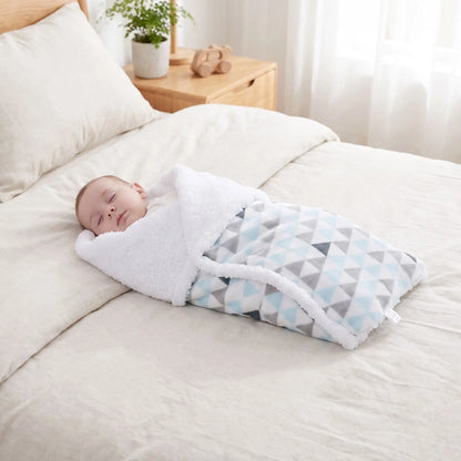 Couverture bébé triangles bleu gris emmaillotant nouveau-né endormi sur lit cosy

