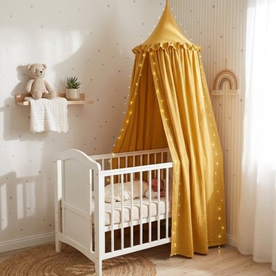 Ciel de lit jaune moutarde à guirlandes lumineuses au-dessus d'un lit bébé blanc