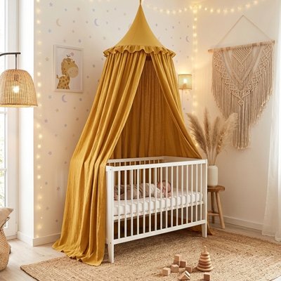 Ciel de lit moutarde au-dessus d'un berceau blanc avec un décor macramé et pampa