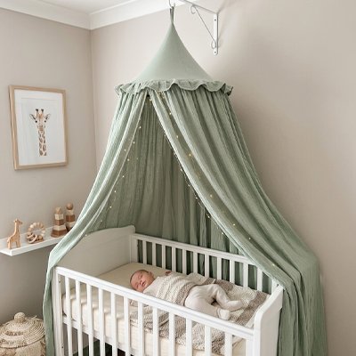 Ciel de lit vert sauge suspendu au mur au-dessus d'un bébé endormi