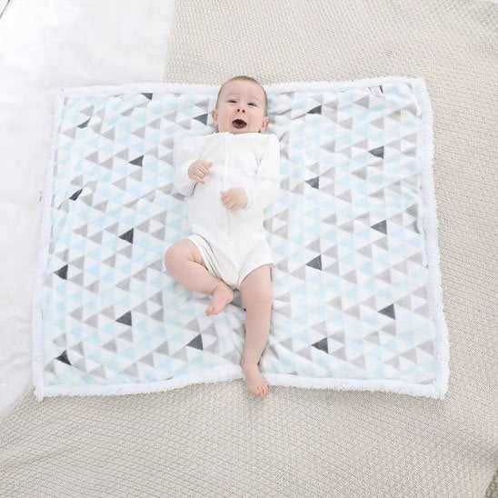 Couverture bébé avec tout-petit souriant allongé sur couverture triangles bleu gris blanc
