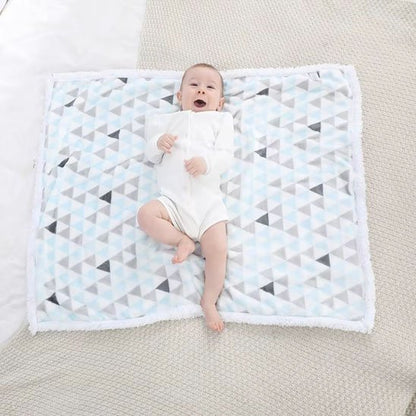 Couverture bébé avec tout-petit souriant allongé sur couverture triangles bleu gris blanc