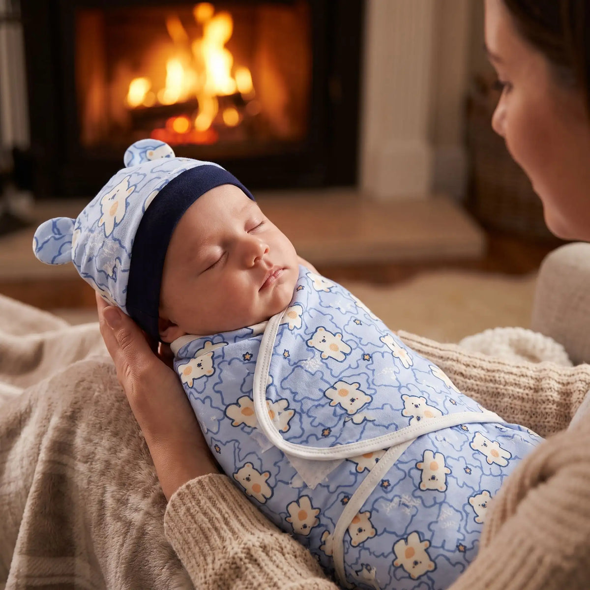 Couverture emmaillotage oursons bleus avec  maman berce son bébé endormi devant la cheminée