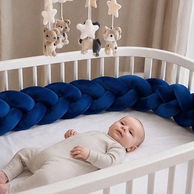 Tour de lit tressé bleu marine avec tout-petit calme allongé sous un mobile