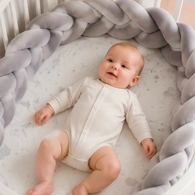 Tresse de lit grise protégeant les bords du berceau avec tout-petit souriant allongé